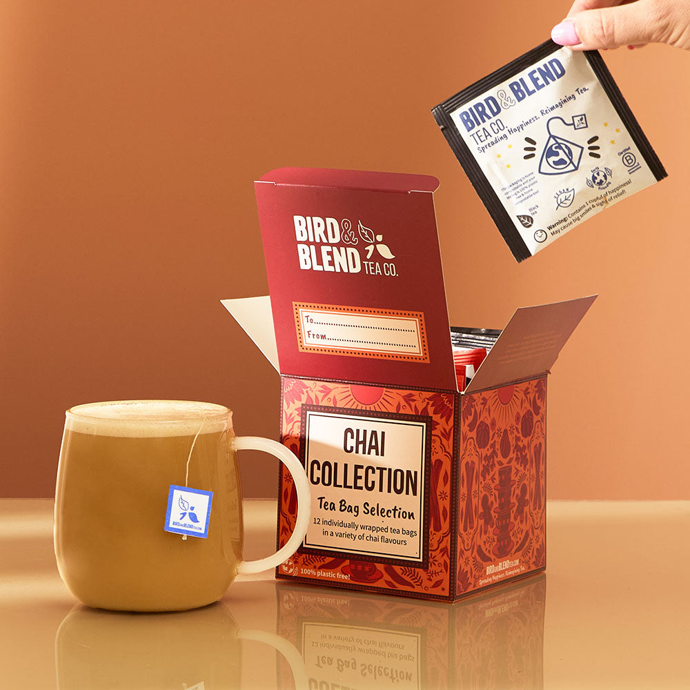 hot chai latte with tea bag in it & chai tea bag gift cube open filled with individually wrapped tea bags & person pulling tea bag out